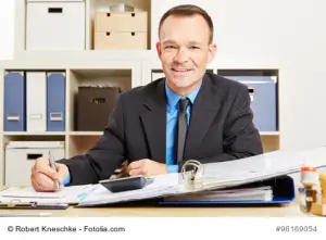 Steuerberater sitzt im Büro am Schreibtisch mit Akten und Taschenrechner